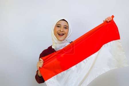 Femme musulmane indonésienne portant le hijab avec un geste fier tout en tenant le drapeau indonésien. Concept de fête de l'indépendance de l'Indonésie