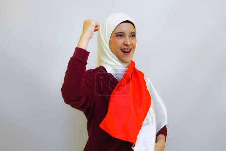 Téléchargez les photos : Femme musulmane indonésienne portant le hijab avec un geste fier tout en tenant le drapeau indonésien. Concept de fête de l'indépendance de l'Indonésie - en image libre de droit