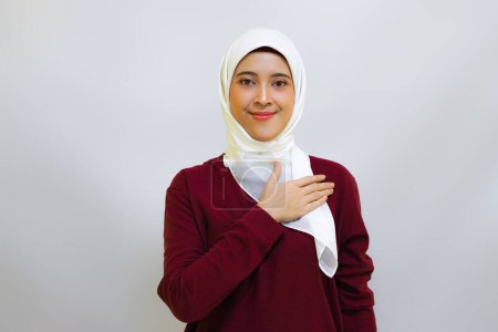 Eine lächelnde asiatische Muslimin mit rotem Oberteil und weißem Hijab, die nach links zeigt, isoliert von weißem Hintergrund. Indonesiens Konzept zum Unabhängigkeitstag