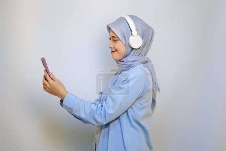 Photo for Happy young Asian muslim woman listening music with headphone. muslim woman advertising concept. listening music concept - Royalty Free Image