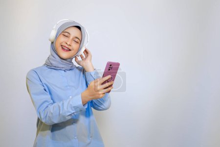 Photo for Happy young Asian muslim woman listening music with headphone. muslim woman advertising concept. listening music concept - Royalty Free Image