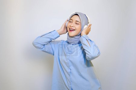 Foto de Feliz joven mujer musulmana asiática escuchando música con auriculares. concepto de publicidad mujer musulmana. escuchar música concepto - Imagen libre de derechos