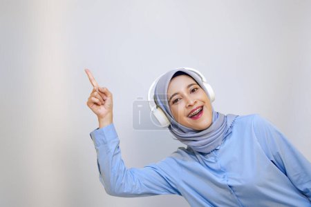 Mujer asiática joven apuntando hacia arriba mientras disfruta de la música en los auriculares. escuchar concepto de música 