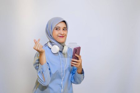 Mujer alegre musulmán con el dedo signo de amor ama la música en su teléfono móvil. auriculares con cable y el concepto de escuchar música 
