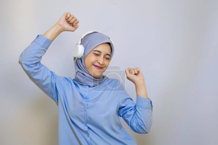 alegre musulmán asiático mujer en azul camisa escuchar música en auriculares