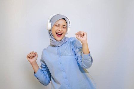 Photo for Cheerful muslim asian woman in blue shirt listening music on headphone - Royalty Free Image