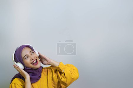 Foto de Chica musulmana feliz en auriculares inalámbricos escuchando música en línea en el teléfono inteligente, disfrutando de una nueva aplicación de fondo blanco - Imagen libre de derechos