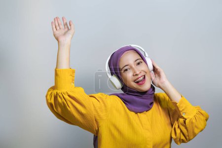 Photo for Happy muslim girl in wireless headphones listening music online on smartphone, enjoying new app white background - Royalty Free Image
