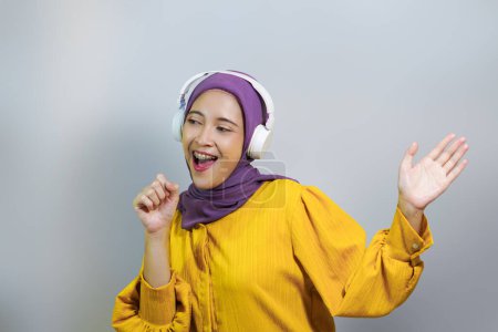 Happy muslim girl in wireless headphones listening music online on smartphone, enjoying new app white background