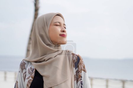Pretty muslim woman enjoying sun shine at the beach wearing cardigan.