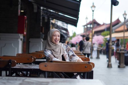 Mujer Hijabi indonesia saludando a distancia o llamando al asistente del café o llamando a su amiga