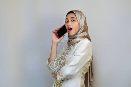 Happy Indonesian muslim woman holding smartphone, pointing camera, and posing for video call during ramadan or eid celebration