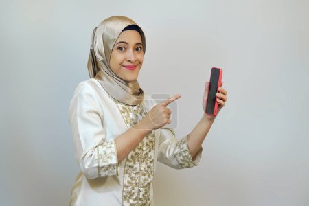 Mujer musulmana indonesia feliz sosteniendo teléfono inteligente, apuntando cámara, y posando para videollamada durante la celebración de ramadán o eid