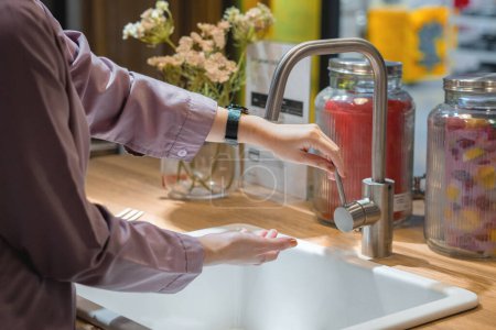 femme en robe violette ouverture robinet à l'évier de cuisine dans sa maison pour se laver les mains