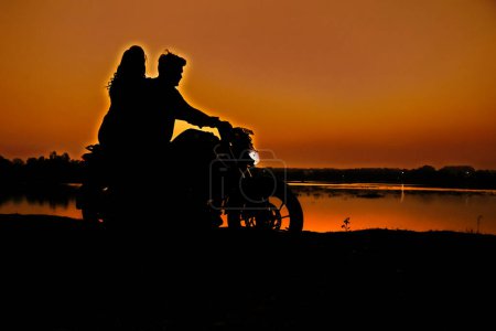 Foto de Silhouette of a love couple on the bike. Orange sunset. Romantic silhouette. Travel couple. Happy Together. He and She. Boyfriend And Girlfriend. Happy Valentine's Day. Love you. - Imagen libre de derechos