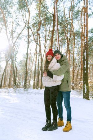 Téléchargez les photos : Les jeunes couples heureux se tiennent debout et s'embrassent par une journée ensoleillée dans un parc enneigé. Portrait d'hommes et de femmes dans un parc hivernal enneigé. Cadre vertical. - en image libre de droit