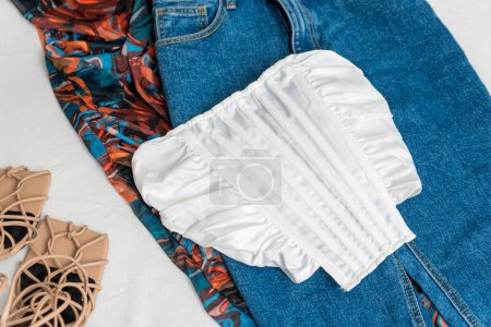 Photo for White corset, blue denims, colored part of clothes and beige sandals on white background. Daily capsule. - Royalty Free Image