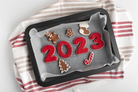 Gingerbread numbers 2023 and Christmas cookies with glazed sugar icing on baking sheet. Traditional baking.