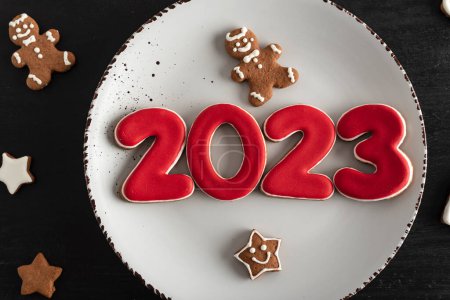 Photo for Top view Tasty glazed painted cookies on white plate: numbers 2023, stars and fir-tree. Close up. New Year food concept. - Royalty Free Image