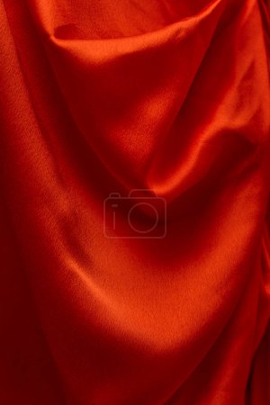 Wellenförmige Textur aus rotem Satinstoff in Nahaufnahme. Seide oder Satin. Textiler Hintergrund. Helles Tuch, vertikaler Rahmen.
