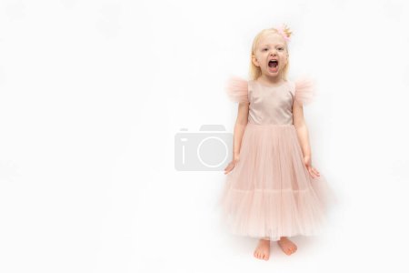 Photo for Little girl in pink lush dress is screaming . Cute girl in elegant dress and bare feet isolated on white background. Capricious girl. - Royalty Free Image