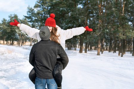 Téléchargez les photos : Happy young couple in love walks in winter forest and fools around. Guy holds his beloved in his arms. - en image libre de droit