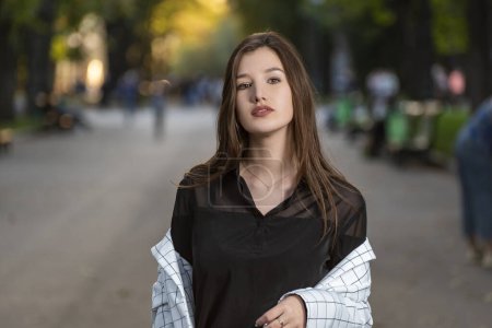 Photo for Young brunette girl with brown eyes and beautiful skin in the background of the park. Portrait of sexy raven-haired - Royalty Free Image