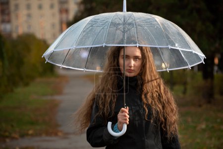 Foto de Jovencita triste con paraguas en el parque. Retrato estacional. Mujer joven con heredero marrón largo bajo paraguas - Imagen libre de derechos