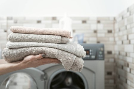 Téléchargez les photos : Les mains des femmes tiennent des serviettes éponge sèches et propres sur le fond de la machine à laver. Lave-serviettes - en image libre de droit