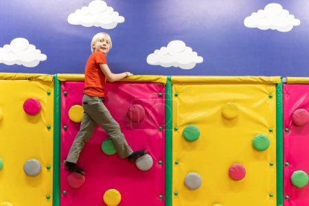 Photo for Blond boy in childrens playroom on climbing wall. Child has fun in the entertainment center - Royalty Free Image