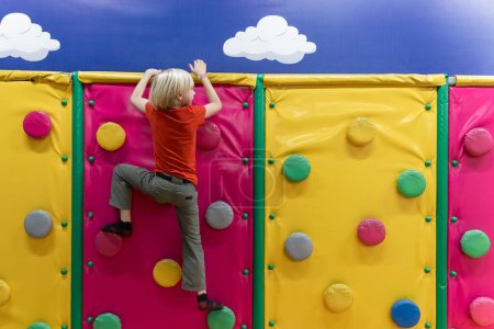Photo for Back view on boy climbs soft climbing wall. Soft room for games.Child has fun in the childrens playroom. - Royalty Free Image