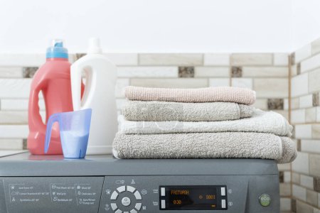 Téléchargez les photos : Produits chimiques ménagers pour le lavage en bouteilles sur la machine à laver et pile de serviettes propres à sec. Laver les serviettes éponge - en image libre de droit