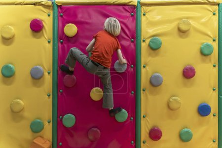 Photo for Boy climbs soft climbing wall. Child has fun in the childrens playroom. Soft room for games - Royalty Free Image