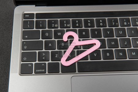 Foto de Percha pequeña de color rosa para la ropa en el teclado portátil. Compras en línea, compra de ropa en Internet. Tienda online de ropa. - Imagen libre de derechos