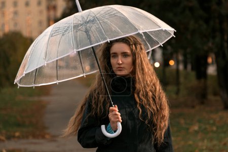 Foto de Chica triste con paraguas en el parque de otoño. Retrato estacional de noviembre. Mujer joven con heredero marrón largo bajo paraguas - Imagen libre de derechos