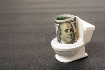 Concepto de desperdicio de dinero, tirar dinero por el inodoro. Billete de dólar en el baño de cerca. Devaluación e inflación del dólar.
