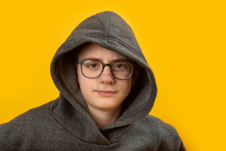 Photo for Portrait of boy with glasses wears hoodie and hood on yellow background. Shy unsociable teenager - Royalty Free Image