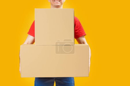 Photo for Man holding large cardboard boxes on bright yellow background. Courier or postman with parcels. Copy space, mock up. Space for text. - Royalty Free Image