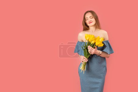 Photo for Beautiful young woman in bare-shouldered dress holding bouquet of yellow flowers isolated on pink background. Copy space - Royalty Free Image