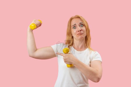 Photo for Upset attractive young woman with dumbbells. Grueling workout, Sporty red hair girl. Pink pastel background - Royalty Free Image