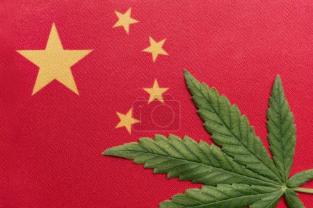 Téléchargez les photos : Grand drapeau de la RPC près et feuille de cannabis frais. Culture et distribution illégales. Usage médical. - en image libre de droit