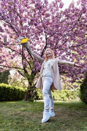 Fröhliche Frau mit einem Strauß gelber Tulpen im blühenden Park. Glückliche Frau mit Blumen im Frühlingspark. Ganzkörperporträt.