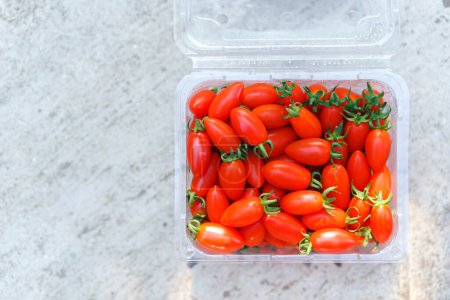 Téléchargez les photos : Tomates cerises dans une boîte en plastique transparent sur un fond en béton, vue de dessus. Espace de copie. - en image libre de droit