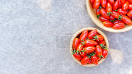 Foto de Fresh red cherry tomatoes in wooden bowl placed on concrete background, top view, copy space. - Imagen libre de derechos
