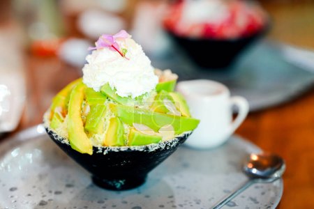 Green avocado bingsu in a black cup and an appetizing spoon on a table in a cafe.