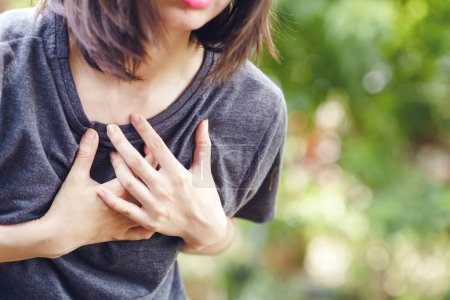Asiatin hat Brustschmerzen, also hält sie ihre Hand vor Schmerzen an ihre Brust. Gesundheitskonzept.
