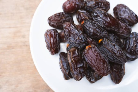 Brown dried Medjool dates in a white plate are sweet and juicy. They are eaten by Muslims during fasting.