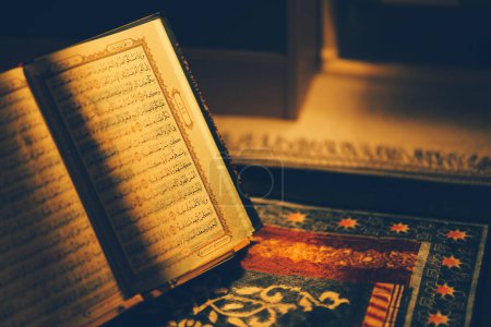 El Corán se abre para la lectura y se coloca en una alfombra de oración y tiene el resplandor dorado del fuego. Enfoque selectivo.