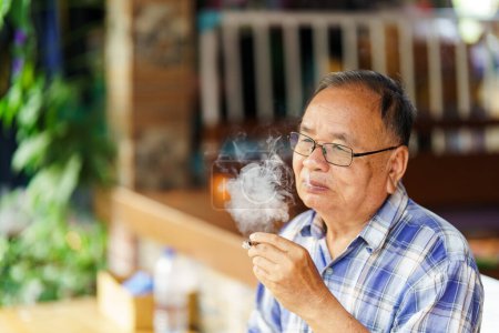 Un anciano fumaba tabaco que emitía humo. El concepto de perjudicar la salud.