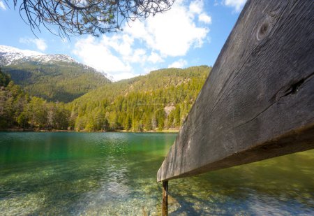 Téléchargez les photos : Garde-corps en bois menant dans l'eau cristalline d'une montagne Lac Tyrol partiellement enneigé paysage de montagne boisé comme un concept pour le temps de loisirs nature intacte et étang de montagne - en image libre de droit